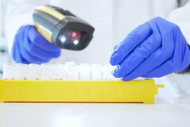 Gloved hands scanning sample tubes with a barcode reader in a laboratory setting